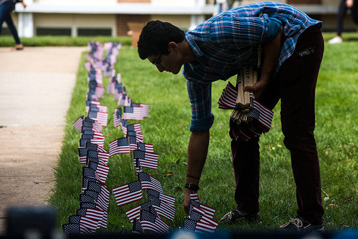 Man places small commemorative flags in the ground along sidewalk