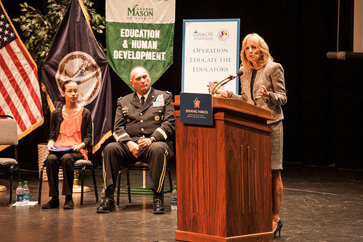 Dr. Jill Biden speaks at podium while military official and student look on
